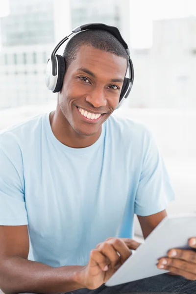 Afro człowiek sobie słuchawki podczas używania cyfrowego tabletu na kanapie — Zdjęcie stockowe