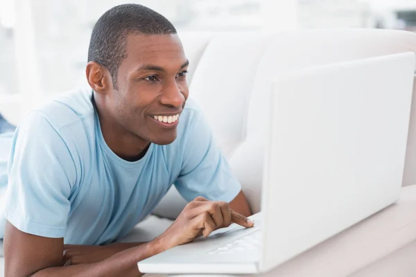Ontspannen casual afro man met laptop liggend op de Bank — Stockfoto