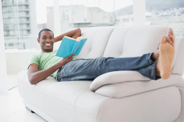 Celovečerní portrét smějící se afro člověka číst knihu na pohovce — Stock fotografie