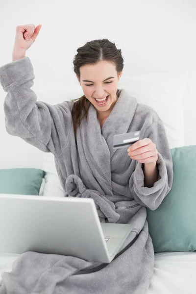 激动的女人，穿着浴袍躺在床上在线购物 — 图库照片