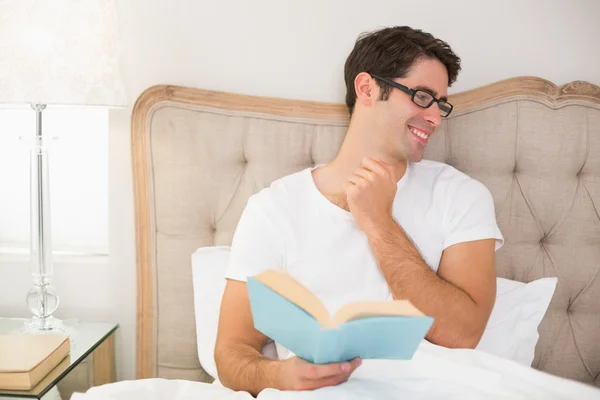 Sonriente hombre relajado leyendo libro en la cama — Foto de Stock