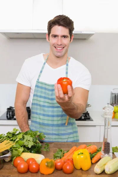 Sorrindo homem segurando pimentão com legumes na cozinha — Fotografia de Stock