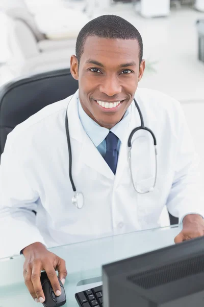 Médecin souriant utilisant un ordinateur au bureau médical — Photo