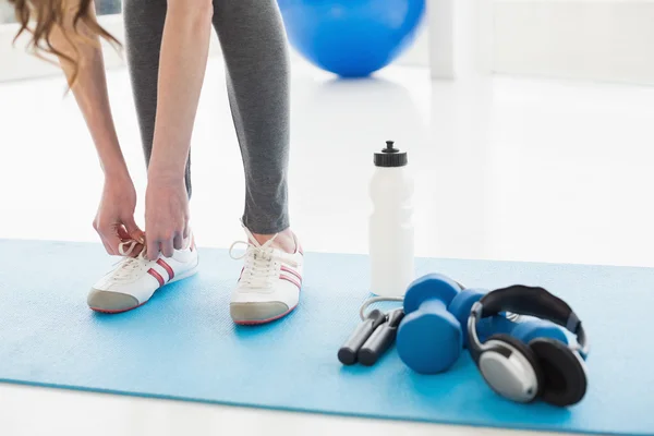 Woman tying shoes with sporty equipment on floor — Stock Photo, Image