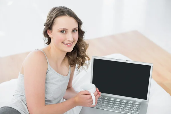 Lässige Brünette mit Kaffeetasse und Laptop im Bett — Stockfoto