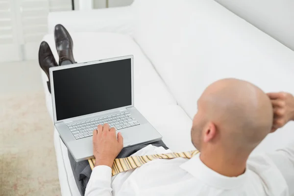 Łysy biznesmen korzysta z laptopa na kanapie w domu — стокове фото