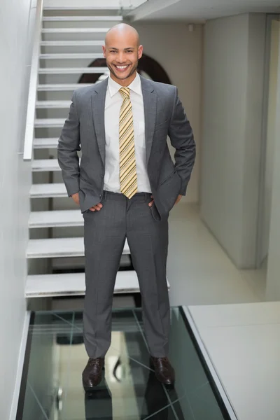 Elegant businessman with arms crossed against staircase in office — Stock Photo, Image