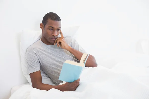 Relajado Afro hombre leyendo libro en la cama — Foto de Stock