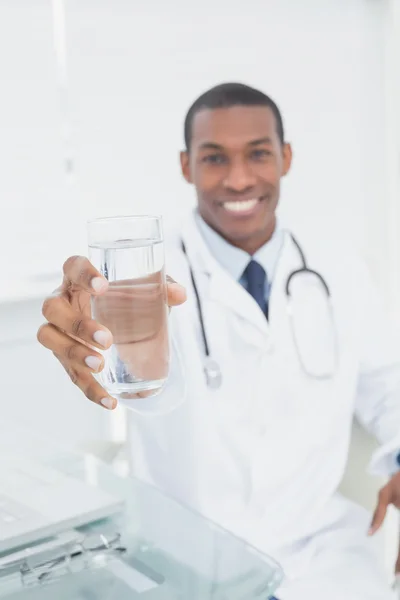 Male doctor holding out a glass of water in medical office — Stock Photo, Image