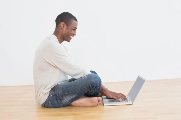 Hombre afro casual usando portátil en el suelo en una habitación vacía — Foto de Stock