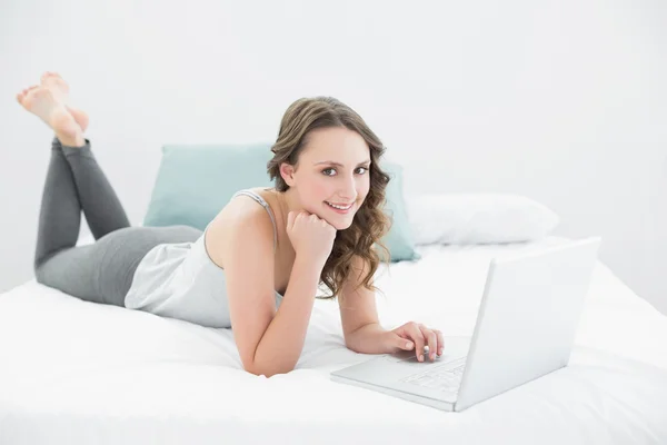 Casual young brunette using laptop in bed — Stock Photo, Image