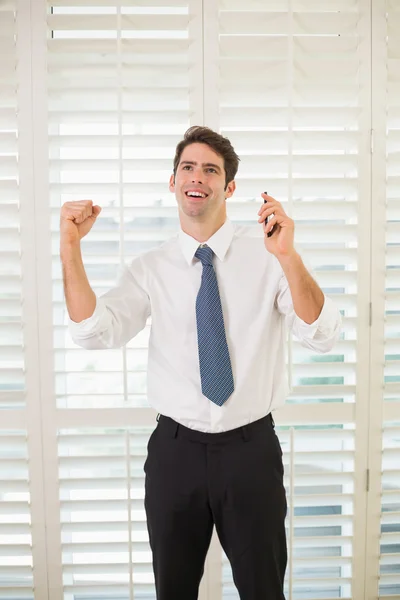 Businessman with mobile phone clenching fist in office — Stock Photo, Image