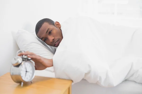 Hombre en la cama extendiendo la mano al despertador — Foto de Stock