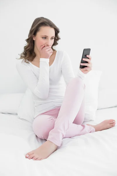 Schockierte Frau mit Handy im Bett — Stockfoto