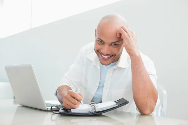 Uomo sorridente casuale con computer portatile che scrive in diario a casa — Foto Stock