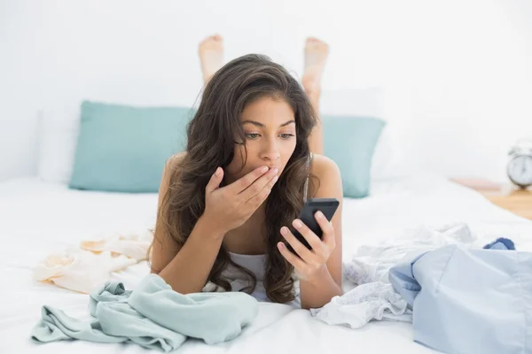Mulher chocada olhando para o telefone celular na cama — Fotografia de Stock