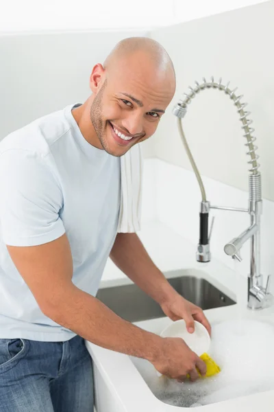 Smiling young man doing the dishes at kitchen sink