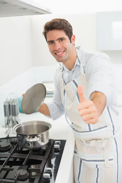 Улыбающийся молодой человек показывает пальцами вверх на кухне — стоковое фото
