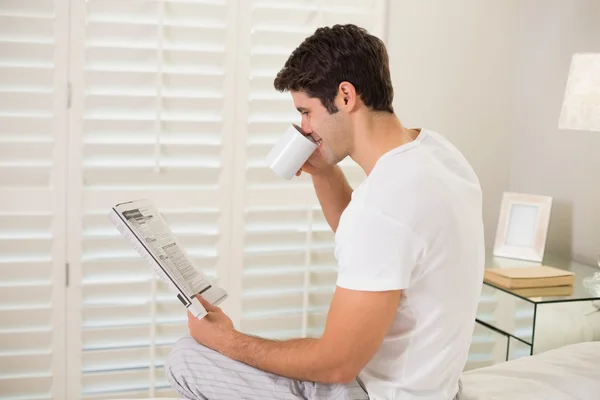 Cheerful man with coffee cup reading newspaper in bed — Stock Photo, Image