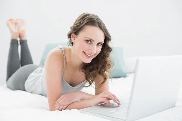 Lässige junge Brünette mit Laptop im Bett — Stockfoto
