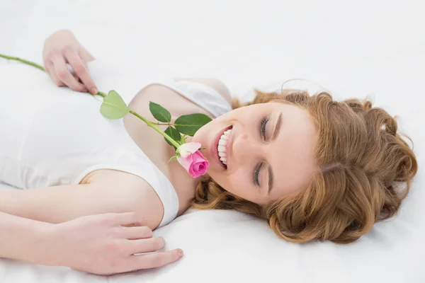 Pretty young woman resting in bed with rose — Stock Photo, Image