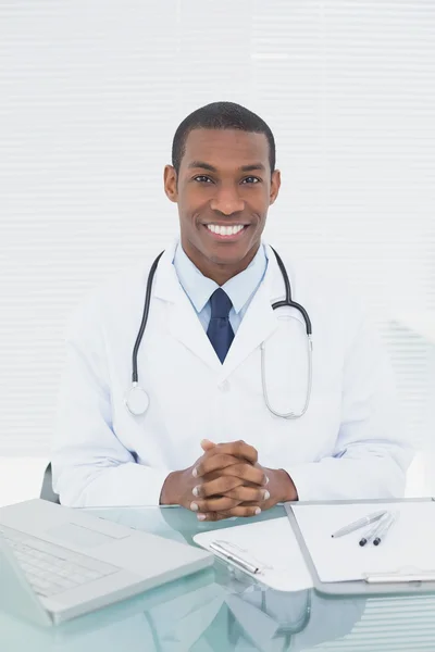 Smilende læge ved hjælp af bærbar computer på medicinsk kontor - Stock-foto