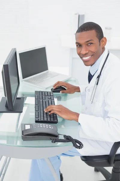 Médecin souriant utilisant un ordinateur au bureau médical — Photo