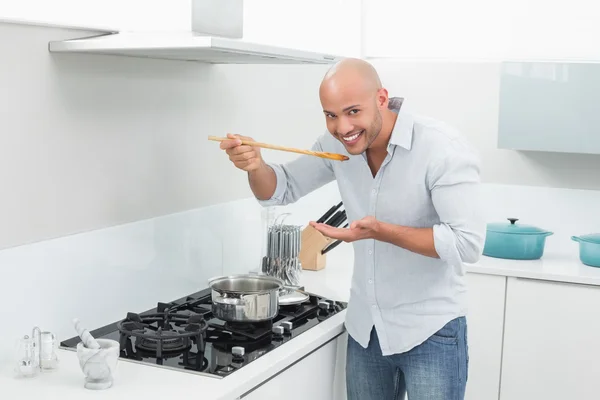 Homem degustação de alimentos enquanto se prepara na cozinha — Fotografia de Stock