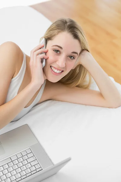 Belle femme blonde téléphonant avec son smartphone couché sur son lit — Photo