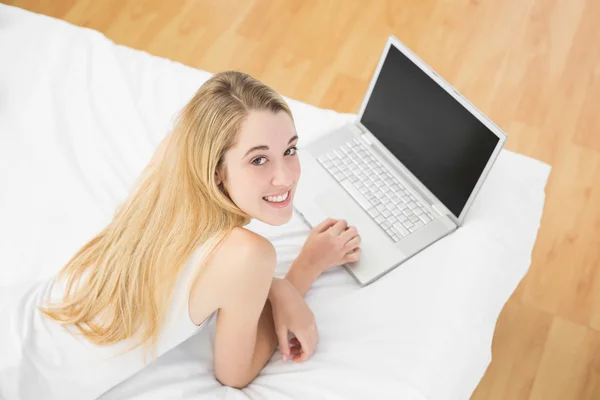 Mujer rubia pacífica trabajando con su cuaderno acostado en su cama —  Fotos de Stock