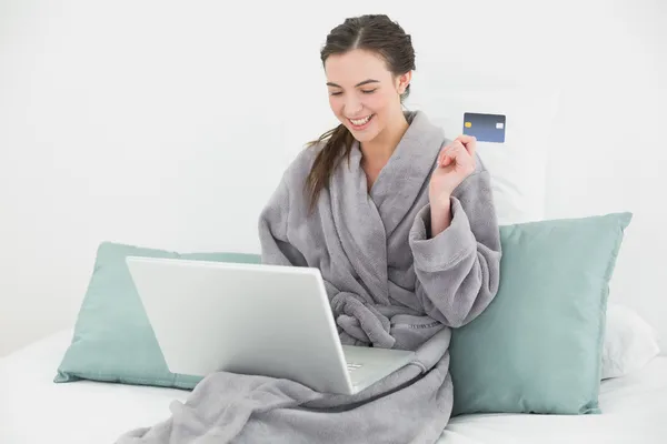 Aufgeregte Frau im Bademantel beim Online-Shopping im Bett — Stockfoto