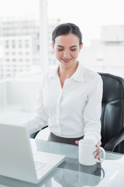 Businesswoman with coffee cup while using laptop at desk — Stock Photo, Image