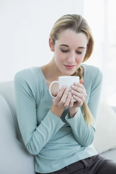 Natural young woman holding a cup sitting on couch — Stock Photo, Image