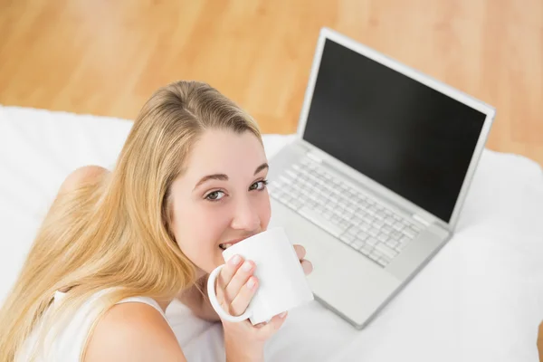 Splendida giovane donna che beve di tazza sdraiata sul suo letto — Foto Stock