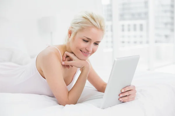 Zufriedene junge Blondine mit Tablet-PC im Bett — Stockfoto