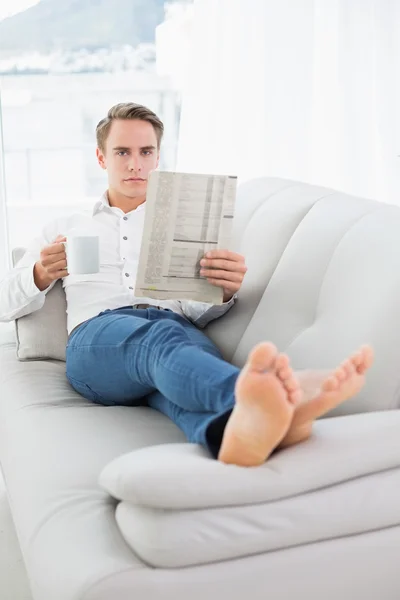 随和的人，一边读报纸，坐在沙发上的喝咖啡 — 图库照片