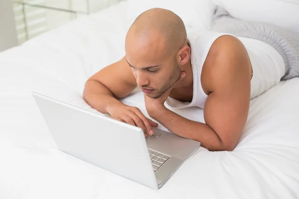 Homem careca casual grave usando laptop na cama — Fotografia de Stock