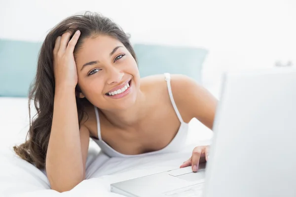 Sonriente mujer casual utilizando el ordenador portátil en la cama —  Fotos de Stock