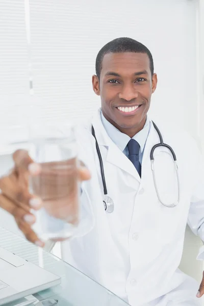 Male doctor holding out a glass of water in medical office — Stock Photo, Image