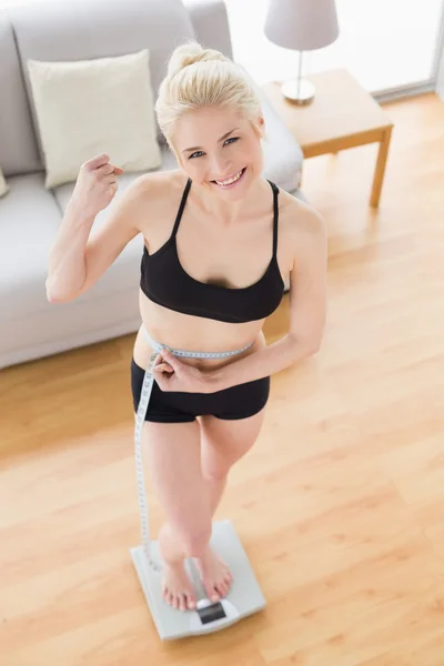 Woman in sportswear standing on scale while measuring waist — Stock Photo, Image