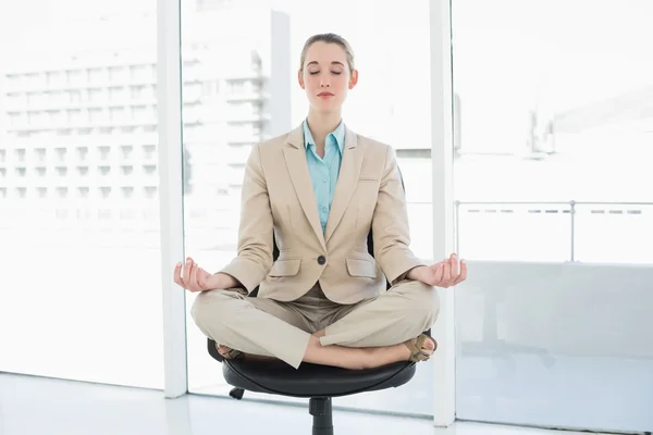 Прекрасная стильная деловая женщина медитирует в позе лотоса на своем поворотном кресле — стоковое фото