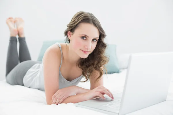 Lässige junge Brünette mit Laptop im Bett — Stockfoto
