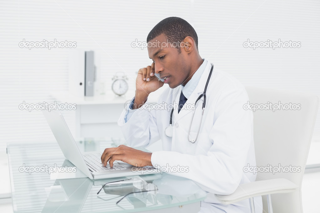 Concentrated male doctor using cellphone and laptop