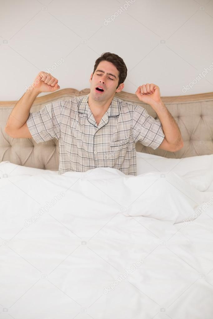 Young man waking up in bed and stretching his arms