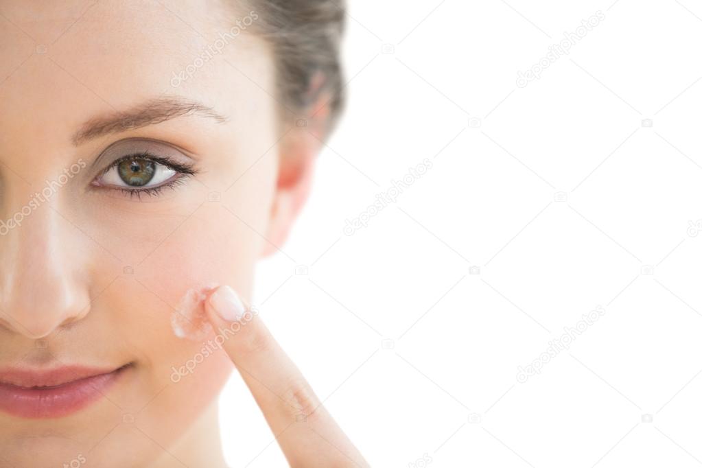 Beautiful young woman applying cream to her face