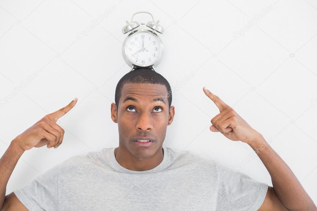 Close up portrait of a man pointing at alarm clock over his head
