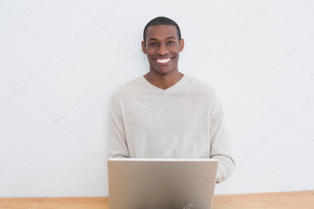 Happy casual Afro man using laptop on floor