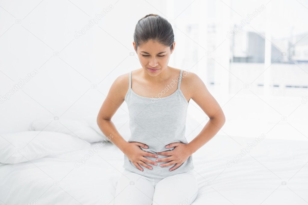 Casual woman with stomach pain sitting in bed