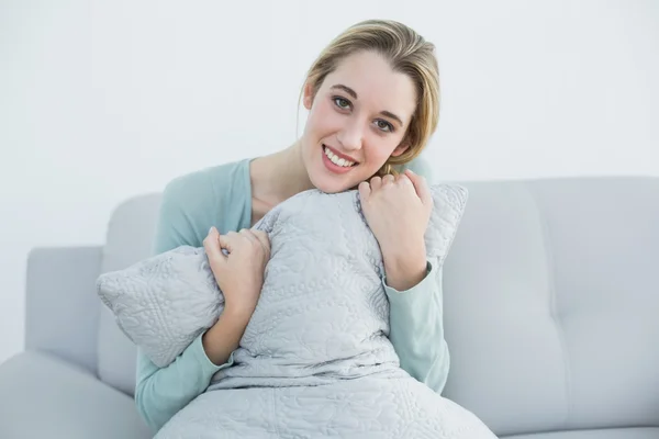 Preciosa mujer sonriente acurrucada con almohada sentada en el sofá —  Fotos de Stock