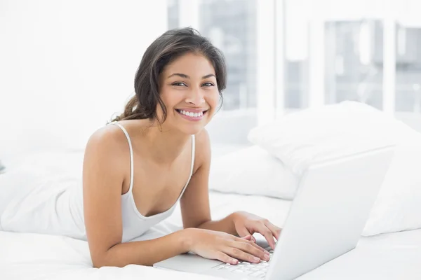 Sorridente casuale giovane donna utilizzando il computer portatile a letto — Foto Stock